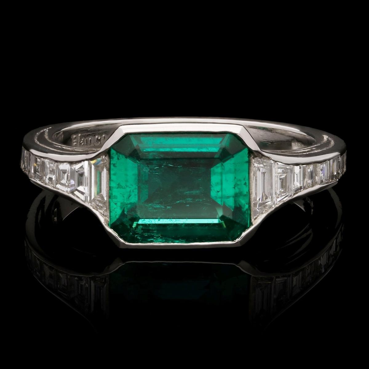 An elegant Colombian emerald ring set in platinum with calibre step-cut diamond shoulders
