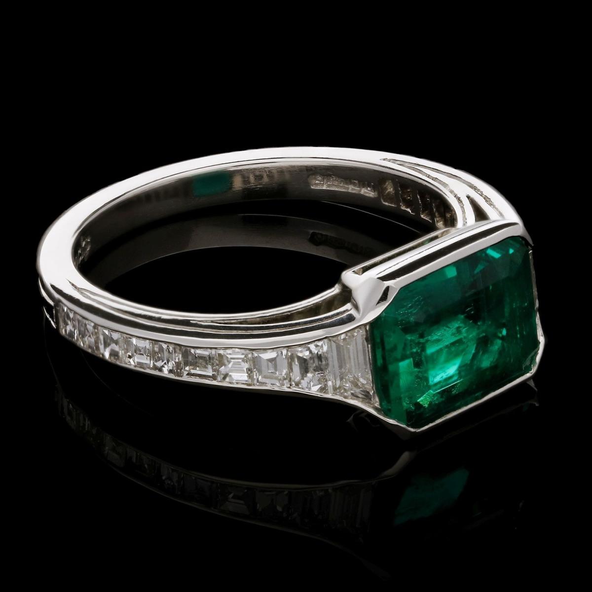 An elegant Colombian emerald ring set in platinum with calibre step-cut diamond shoulders