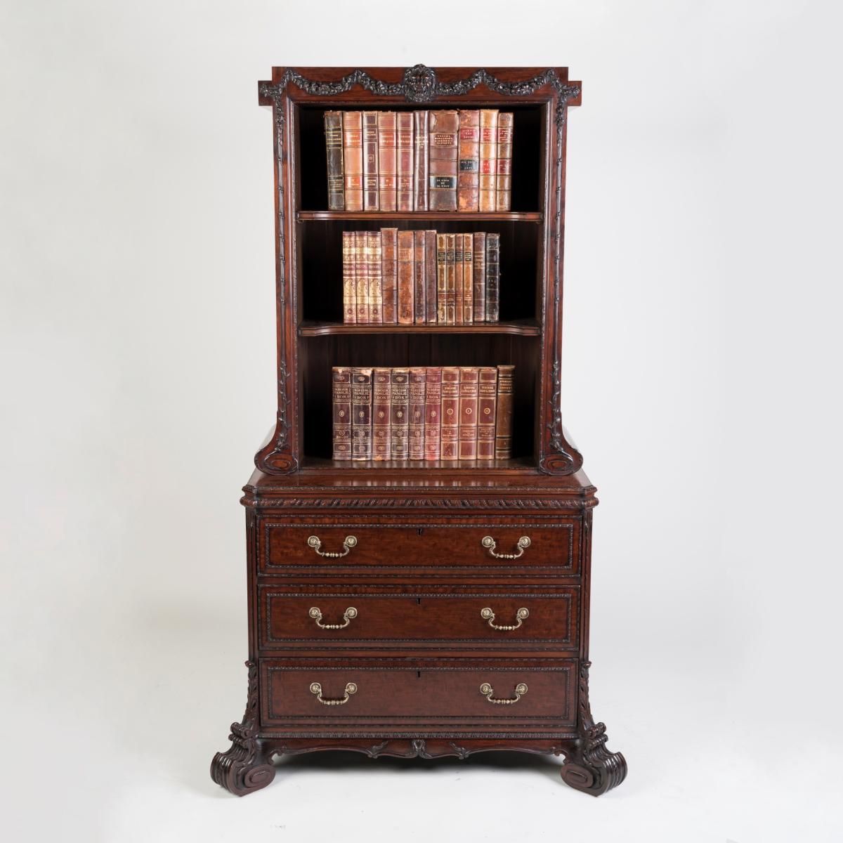 Designed in the neo-classical fashion pioneered by Thomas Chippendale, the mahogany cabinet bookcase is crisply carved throughout, rising from voluminous scrolling supports; the canted sides with acanthus leaf carved decoration and flanking the lockable graduated drawers with brass swan neck handles, the superstructure rising from scrolls in conforming style and enclosing a three-shelved upper cabinet; the cornice applied with carved floral garlands and a central lion’s mask. Stamped to the rear 'H. Samuel,
