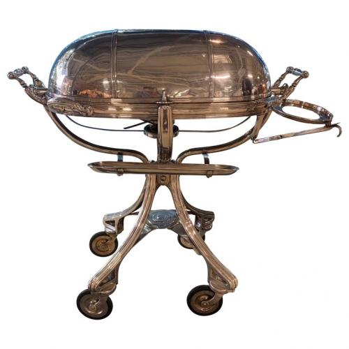 A large Silver plate carving trolley or Roast Beef trolley on four wheels with a hinged lid, which opens to the hot water plate and two compartments inside for accompaniments such as vegetables and gravy.  There is also an interior shelf for carving knives and other utensils. The trolley has two large handles, an underneath burner and a side hinged stand for the plates.