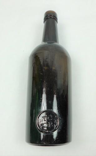 A black glass wine bottle with seal TCCR - Trinity College Common Room